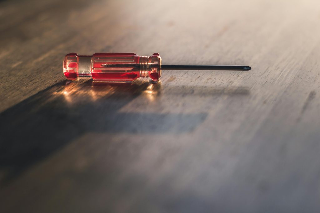 A red screwdriver lies on a wooden surface, highlighting its metallic and transparent handle.